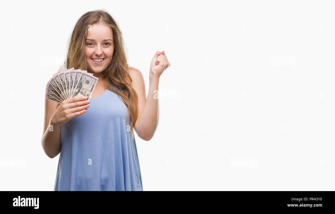 Young blonde woman holding dollars screaming proud and celebrating victory and success very excited, cheering emotion Stock Photo