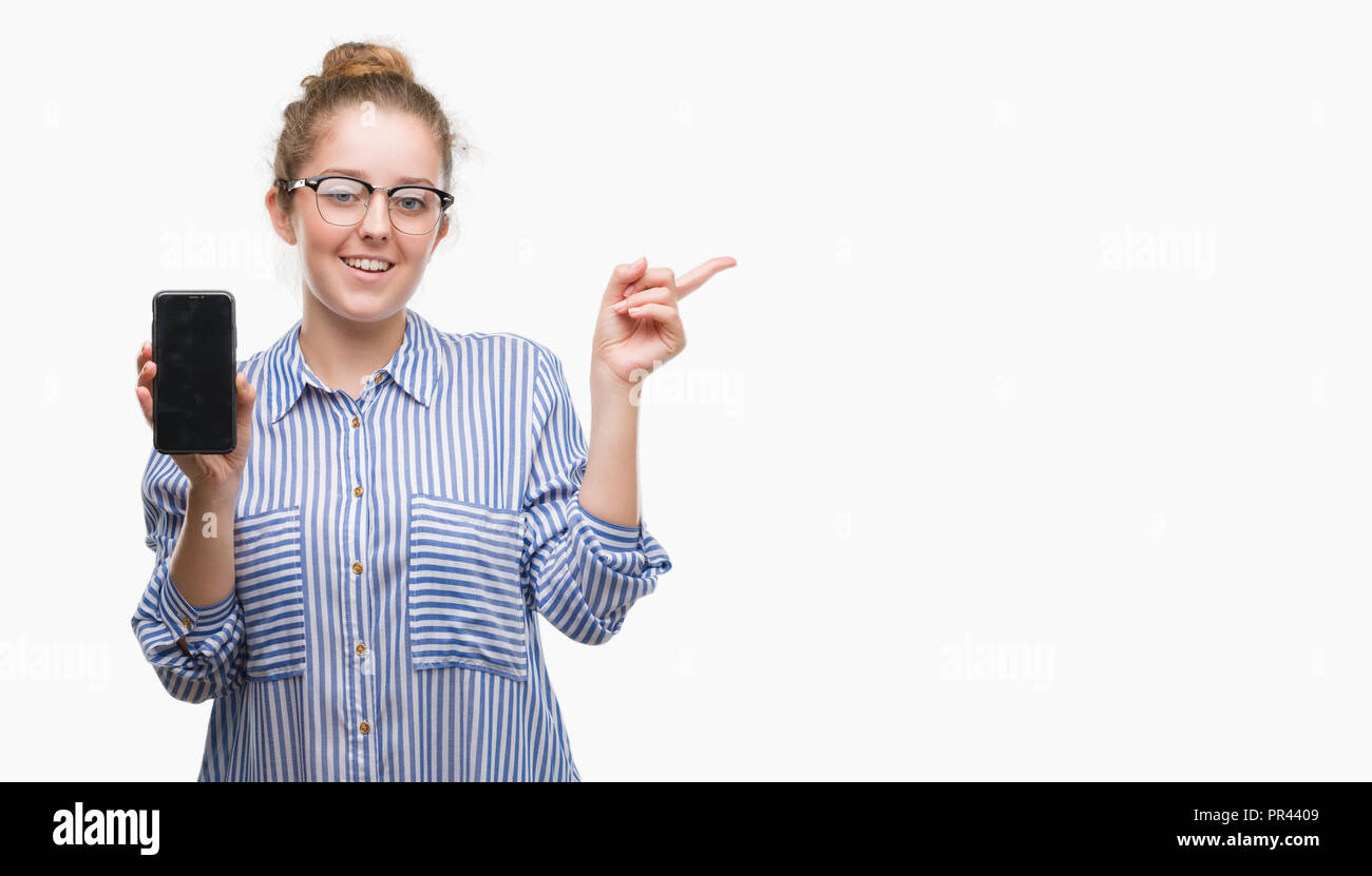 Young blonde woman using smartphone very happy pointing with hand and finger to the side Stock Photo
