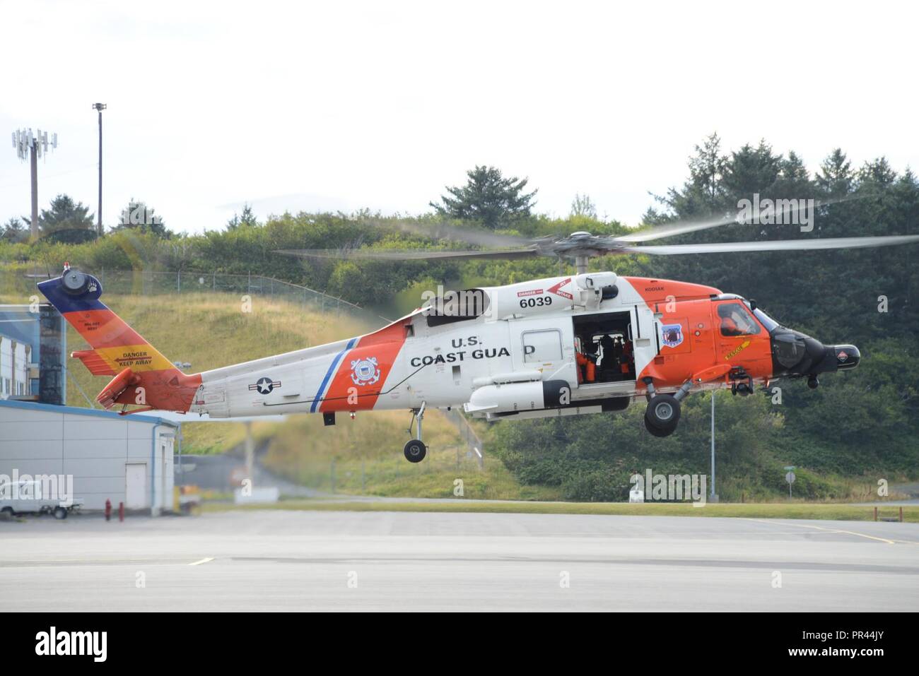 A Coast Guard Air Station Kodiak MH-60 Jayhawk helicopter aircrew hovers above the Air Station Kodiak, Alaska, tarmac before taking off for a training flight Sept. 6, 2018. Training flights ensure aircrews are proficient in emergency procedures and maintain qualifications so they are ready and responsive during search and rescue cases. U.S. Coast Guard Stock Photo