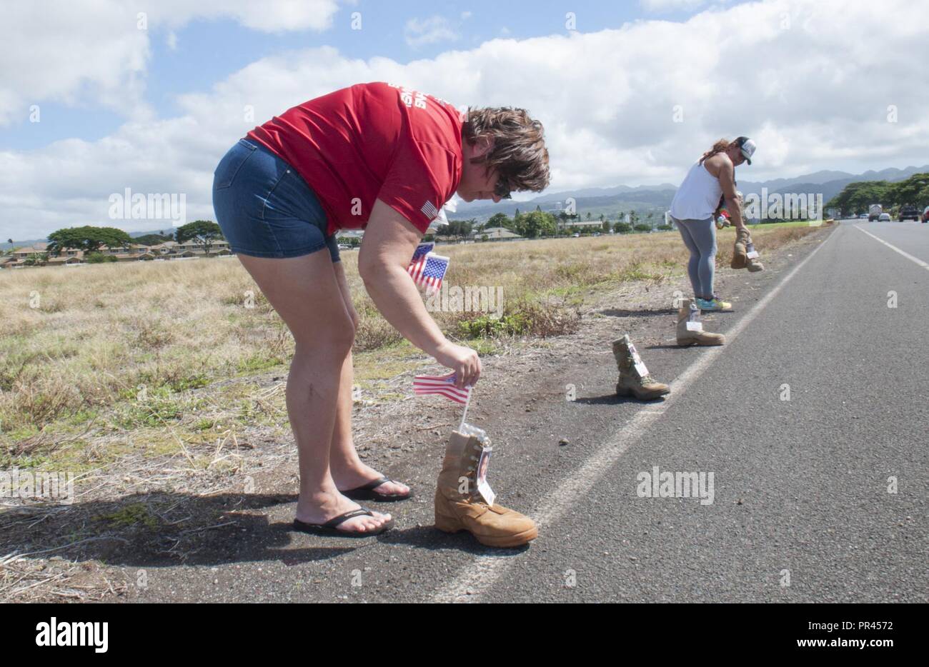 FORD ISLAND — Air Force spouse Kim Andrews (left) places an American flag in each of the many military boots that volunteers like Army spouse Elba Williams (right) have placed along the road at Ford Island, Sept. 6, 2018. The boots, each bearing the name of a fallen service member or military working dog, will line the path for the Fisher House 8K Hero & Remembrance Run, Walk or Roll, scheduled for Saturday, Sept. 8. The boots will be displayed through Sept. 15, 2018, on the corner of O’Kane Blvd. and Enterprise Street. Stock Photo