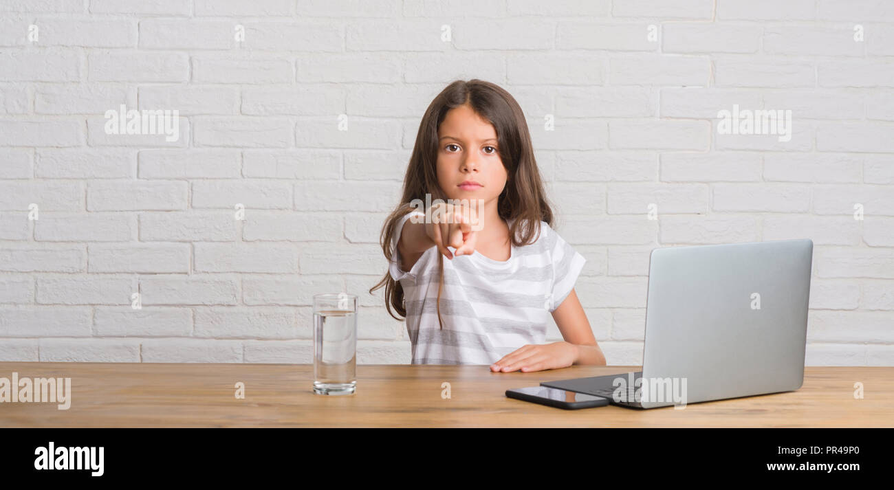 Young hispanic kid sitting on the table using computer laptop pointing ...