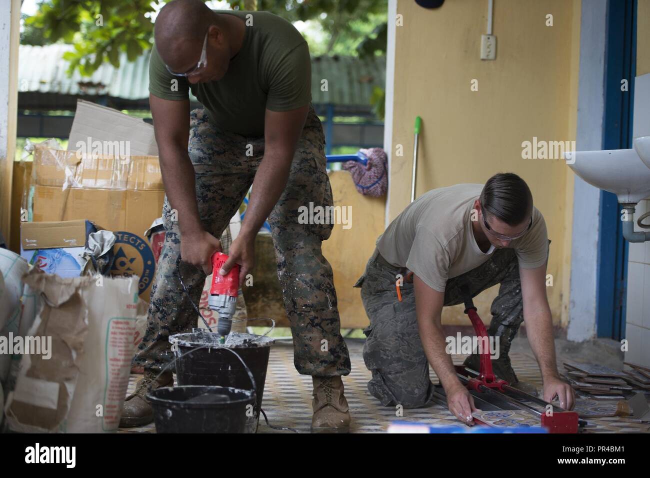 (Left) U.S. Marine Corps Sgt. David Tyson, 7th Engineer Support Battalion combat engineer, mixes grout as U.S. Air Force Staff Sgt. Zach Julian, 145th Airlift Wing water and fuel system maintenance craftsman, cuts tile during Pacific Angel (PAC ANGEL) 18-2 at Nguyen Hien Junior High School in in Phu Thinh town, Phu Ninh district, Vietnam, Sept. 11, 2018. During PAC ANGEL 18-2 civil engineers worked on repairs, refurbishing and upgrades to eight existing rural medical and school facilities. PAC ANGEL is a multilateral humanitarian assistance civil military engagement, which improves military-to Stock Photo
