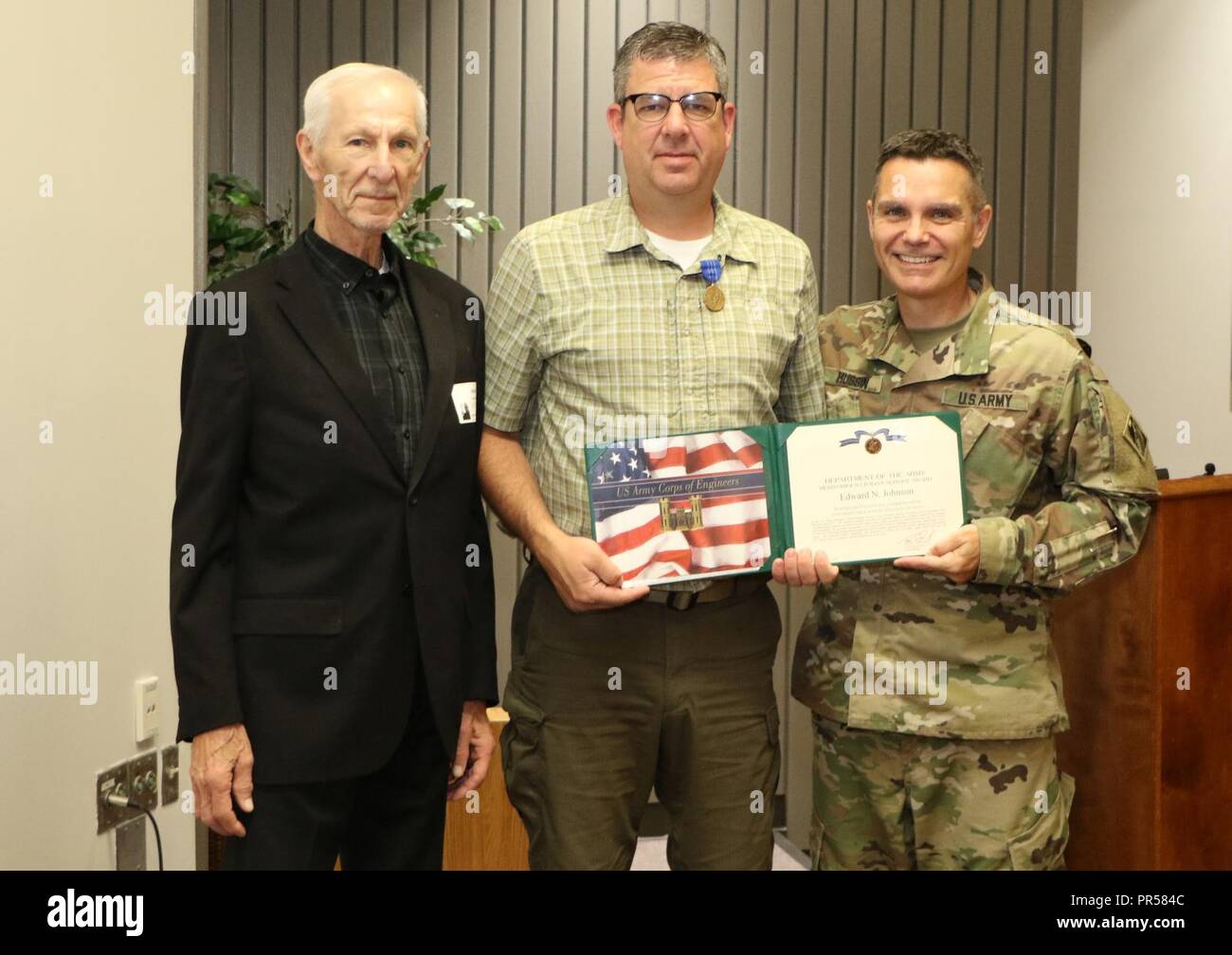 Col. Christopher A Hussin, Commander, U.S. Army Corps of Engineers, Tulsa District, presents Edward N. Johnson (center) the Meritorious Civilian Service Award for his performance while serving as a senior strategic communications advisor to Ukraine’s Minster of Defense from 2016 to 2017. Johnson’s father Harvey (left) was also in attendance during the ceremony. The Meritorious Civilian Service Award is the second highest award granted by the Secretary of the Army or a major Army commander to civilian personnel. Stock Photo