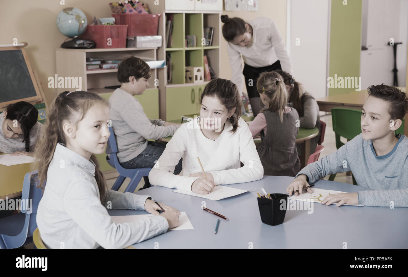 Children elementary age drawing at class, woman teacher helping Stock ...
