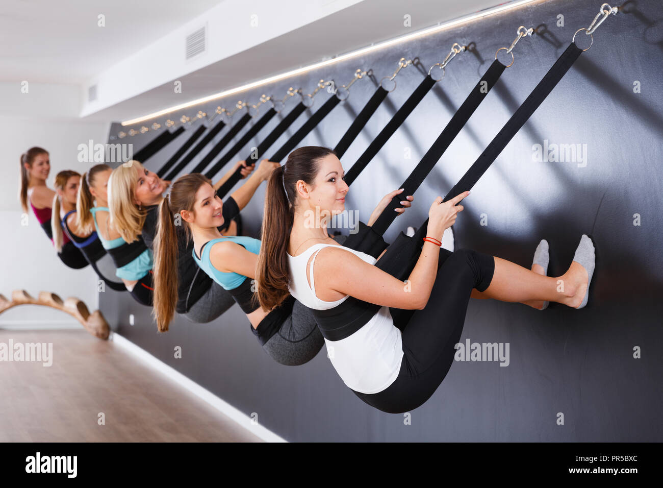Group of sporty girls practicing wall yoga poses with straps in modern yoga  studio Stock Photo - Alamy