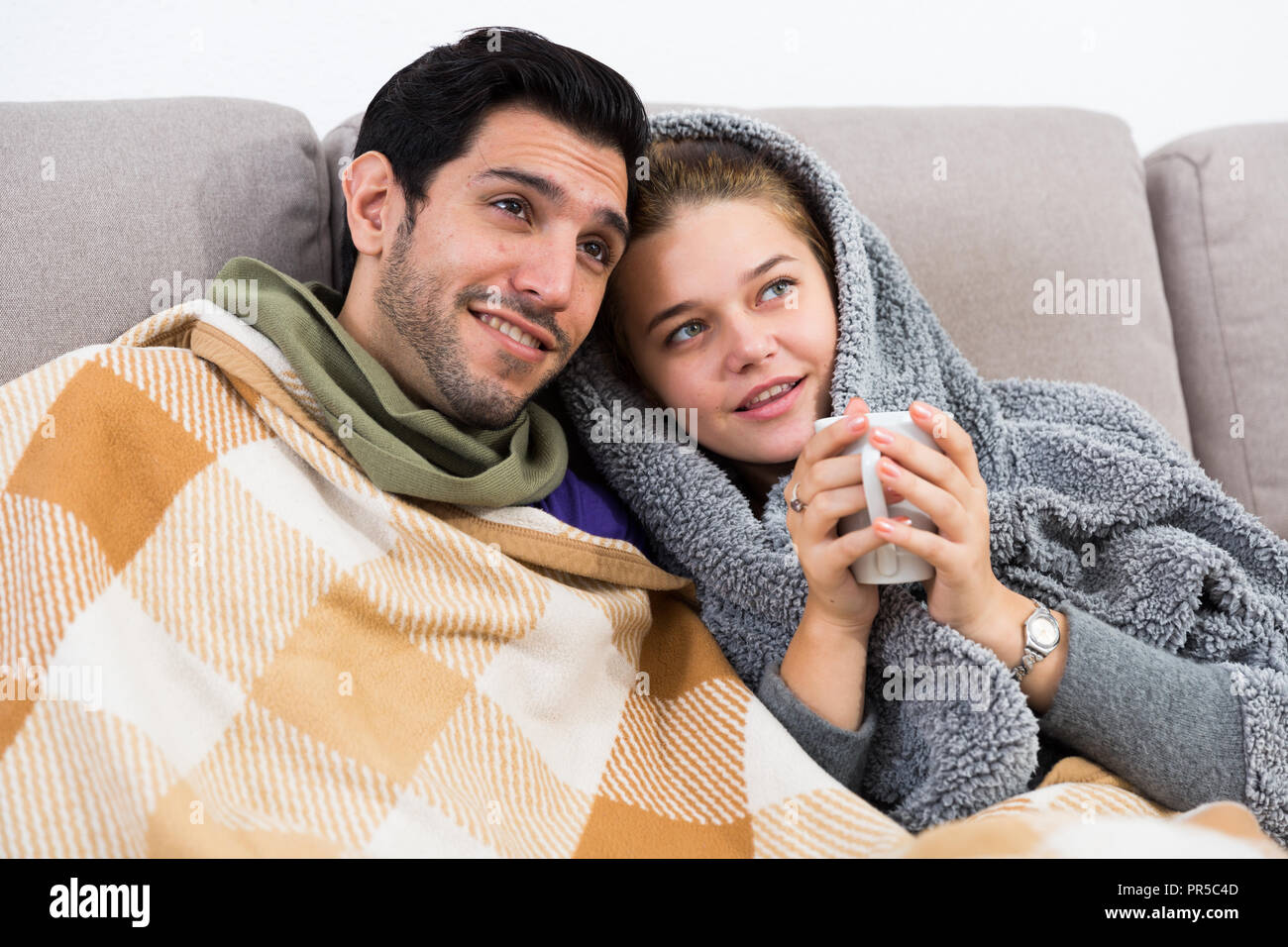 Loving Young Couple Snuggling On Sofa With Cup Of Tea Watching Tv