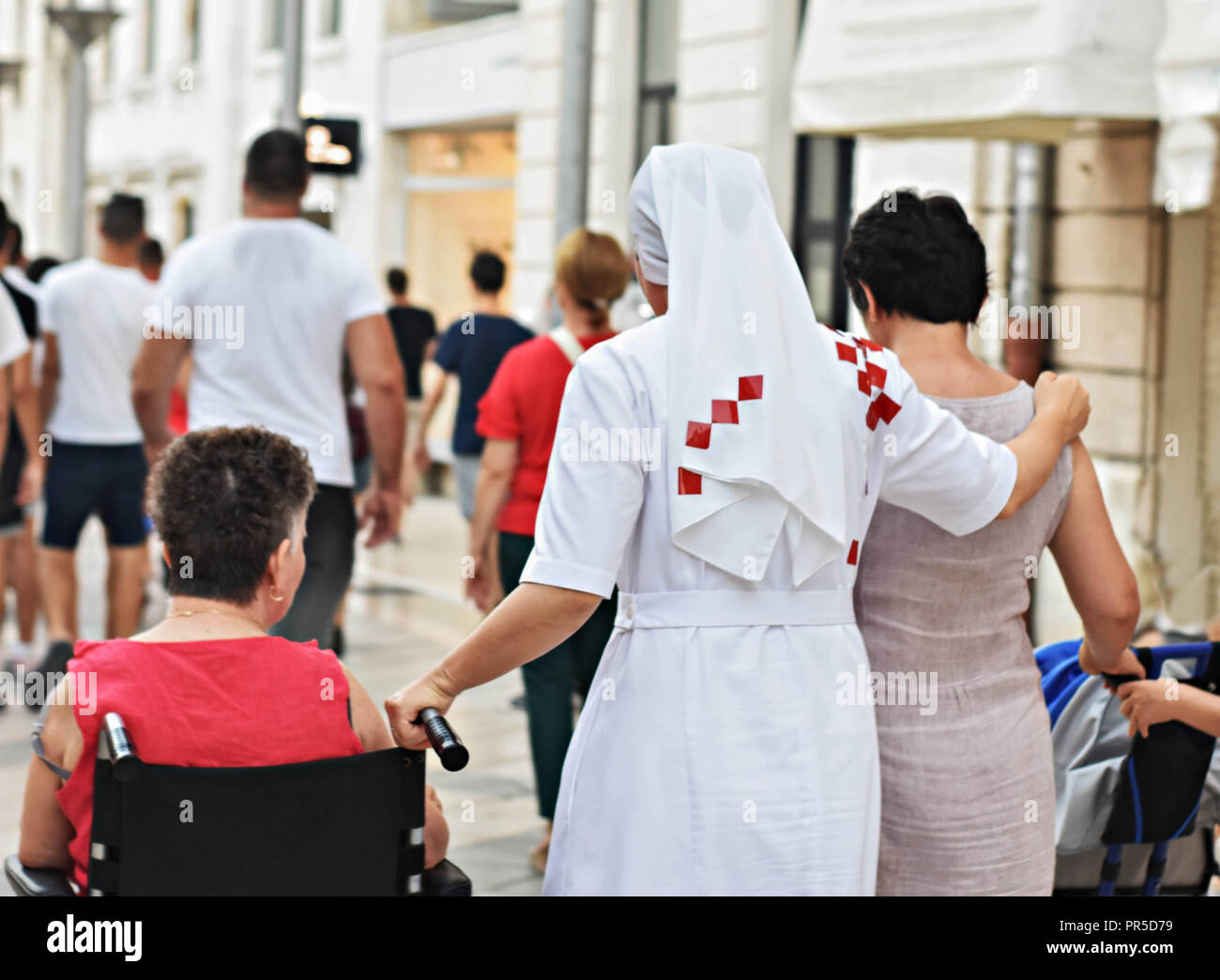 Christian nun walking down the street and helping woman in wheelchair Stock Photo