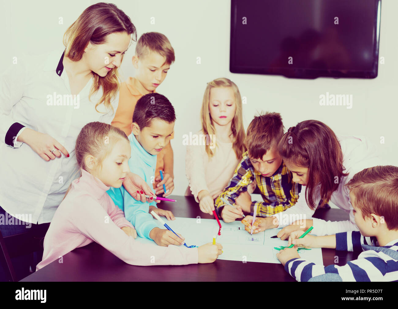Little cute smiling children with teacher drawing together in classroom ...