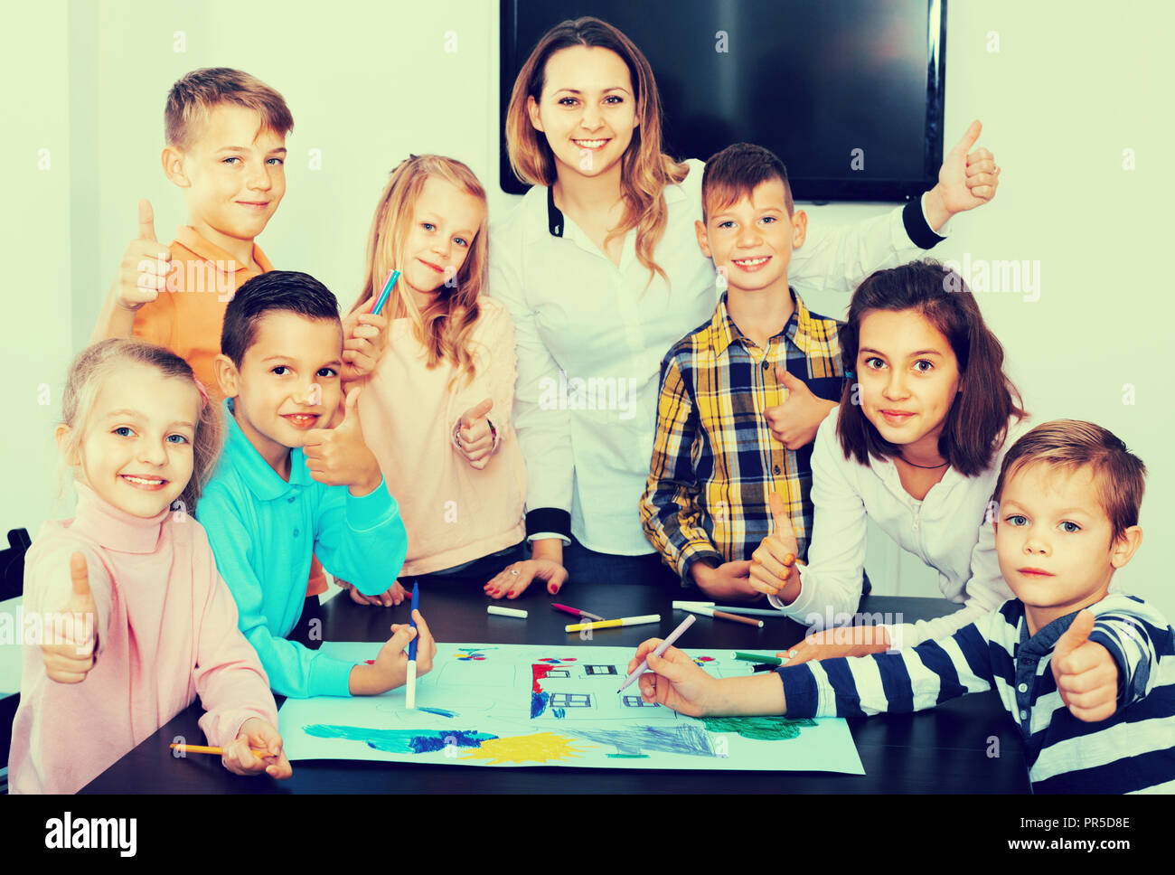 Cute happy smiling children with teacher drawing together in classroom ...