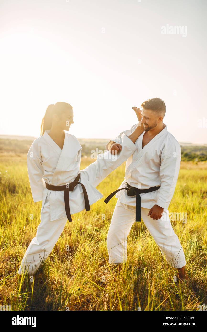Female karate doing stretching exercise on training with male instructor. Martial art workout outdoor, technique practice, self defense Stock Photo