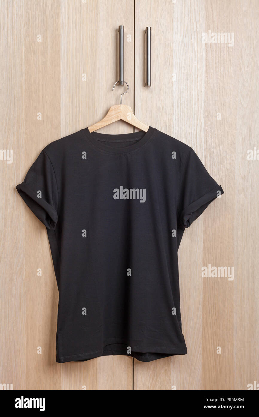 Wrinkled black plain short sleeved cotton T-Shirt hanging on a wardrobe door handle Stock Photo