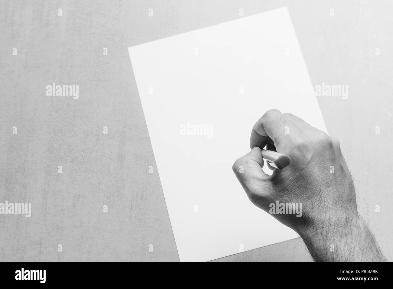 male hand with a ballpoint pen and a blank white sheet of paper on grey ...
