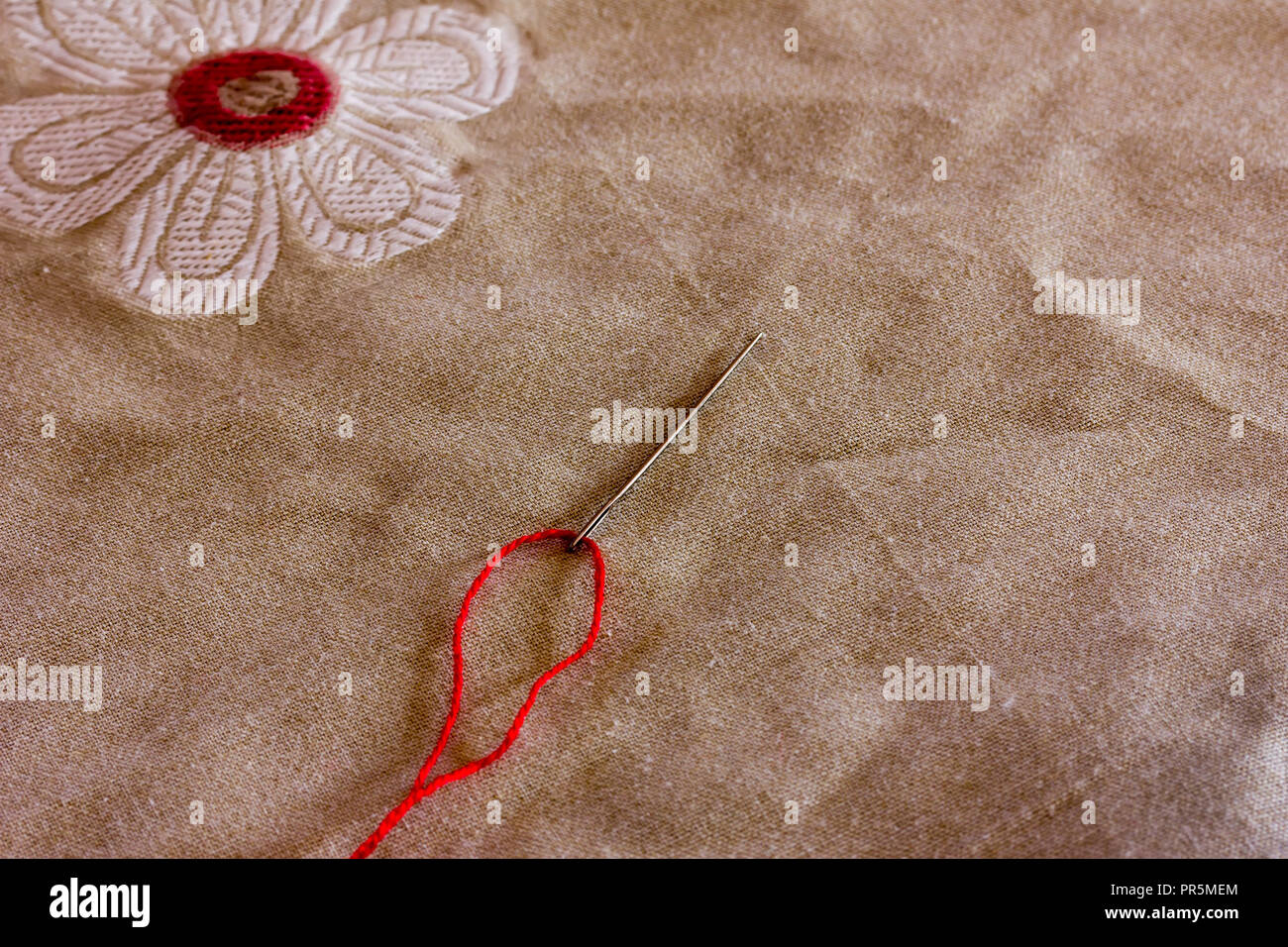 red thread inserted into a needle on the background of linen fabric ...