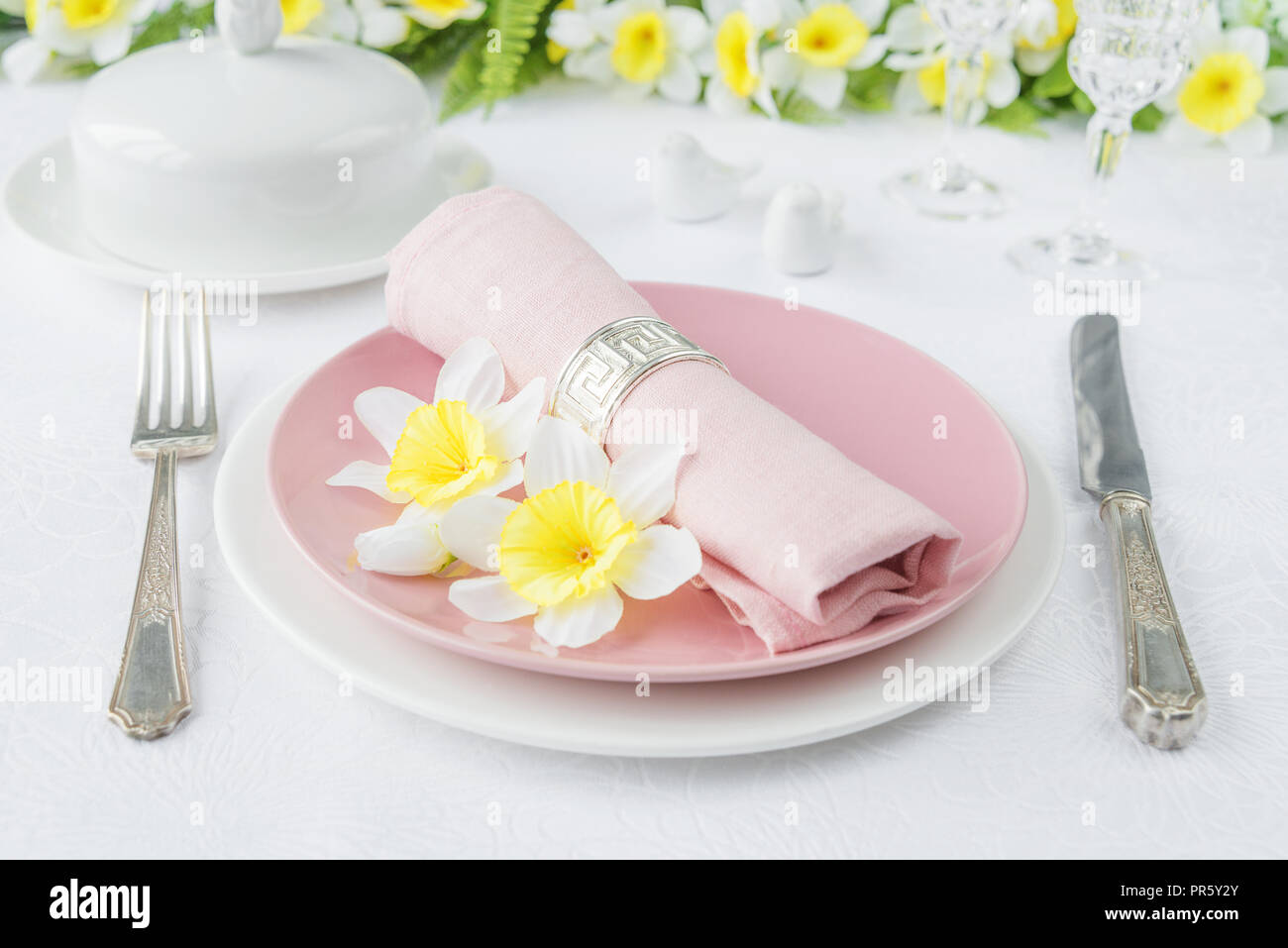 Classic serving for a Easter dinner with white and pink porcelain plates, silverware and spring flowers on a white tablecloth Stock Photo