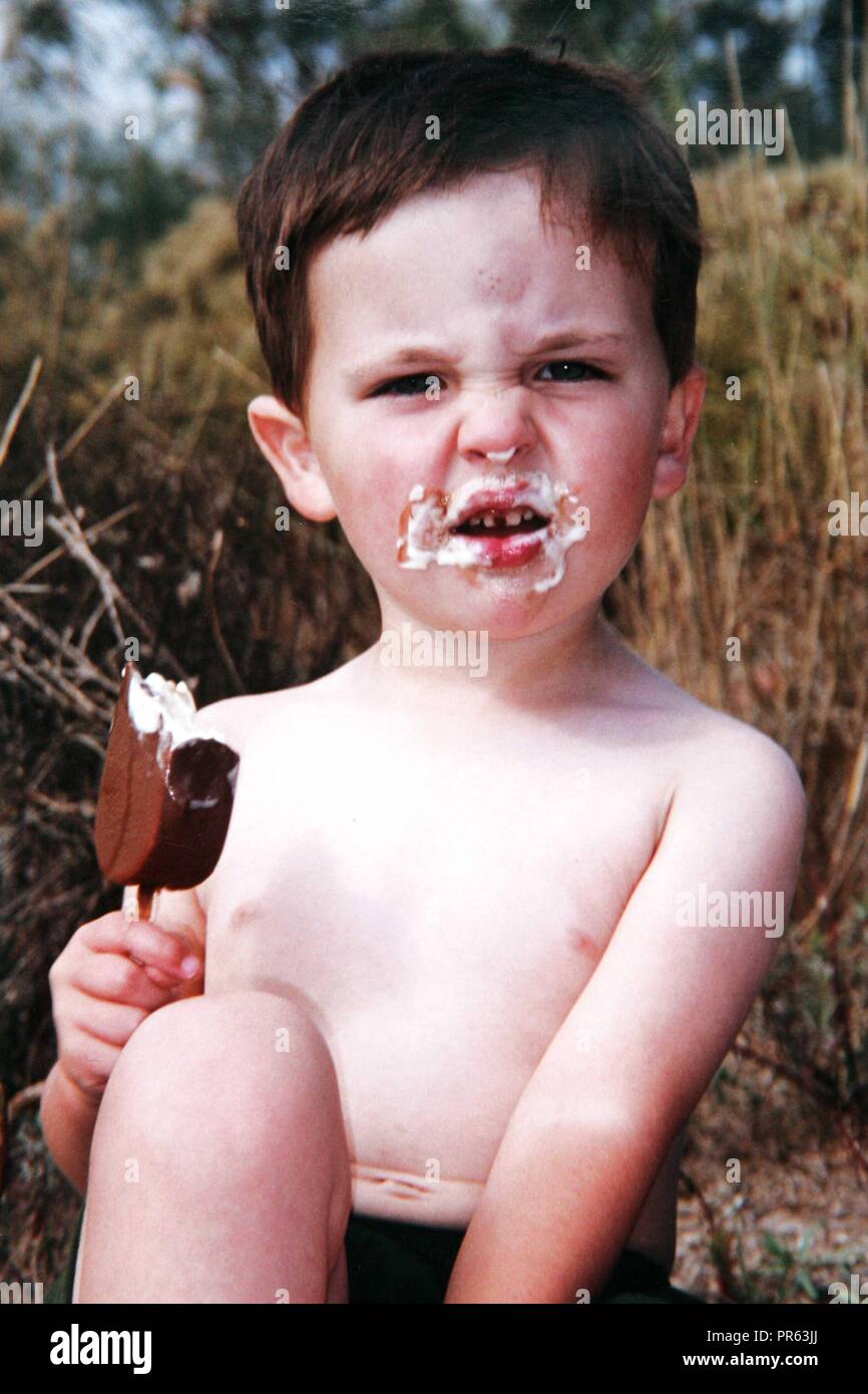 Boy eating ice lolly with ice cream all over face Stock Photo