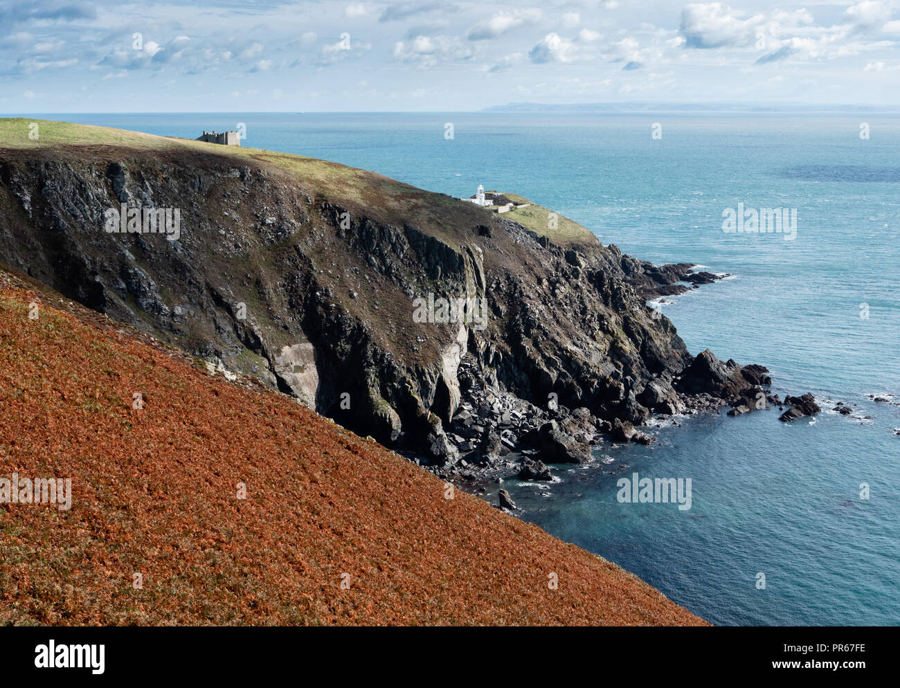 Rugged south coast of Lundy island looking towards Marisco Castle and South Light lighthouse with the Devon coast on the far horizon Stock Photo