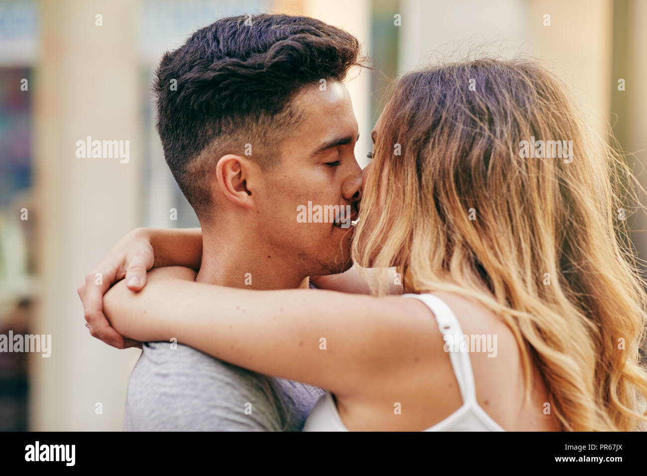 Affectionate young couple sharing a romantic kiss while standing in each other's arms on a street in the city Stock Photo