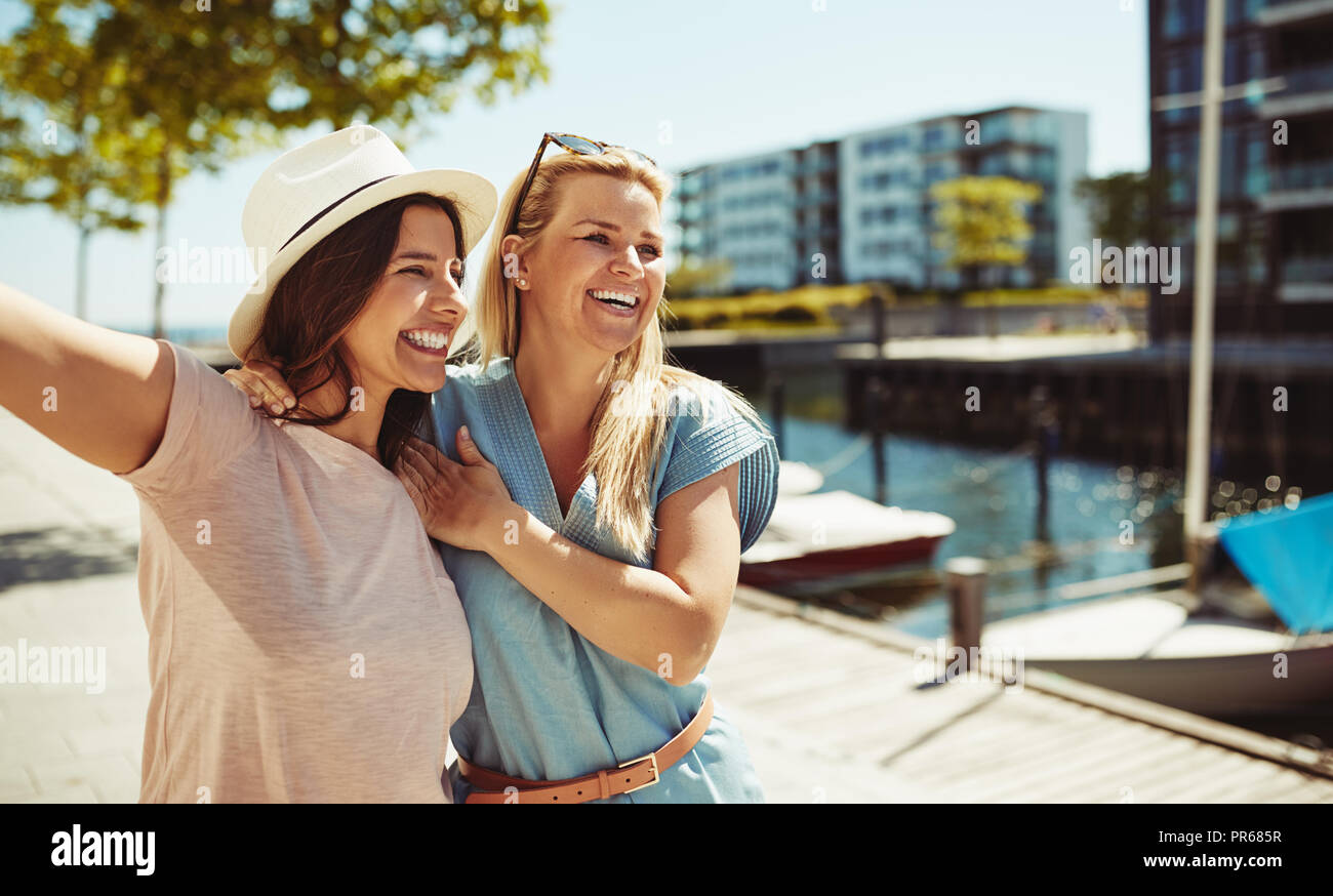 Two carefree young female friends laughing while enjoying a sunny day walking together in the city in summer Stock Photo