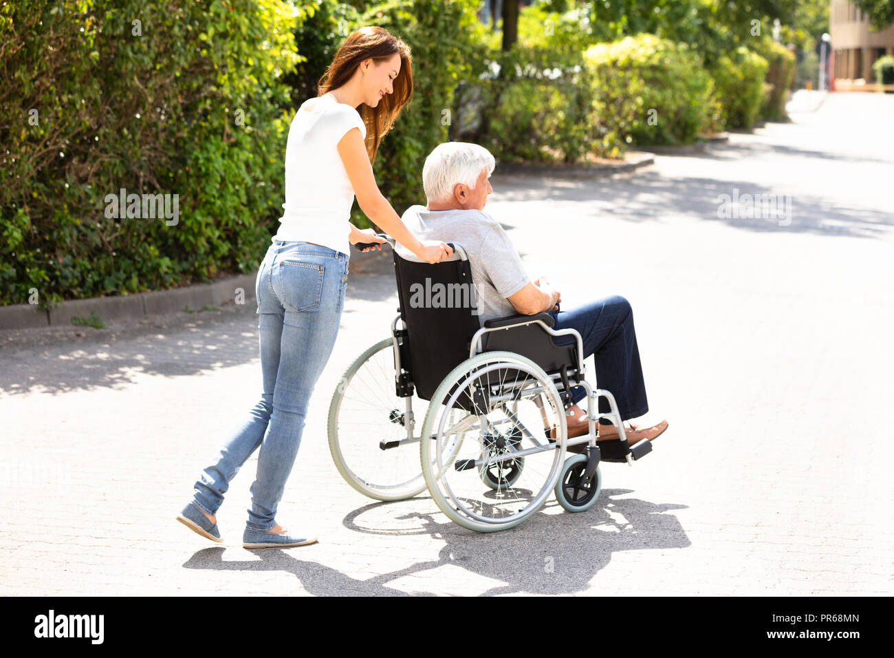 Young Woman Assisting Her Disabled Father On Wheelchair At Outdoors Stock Photo