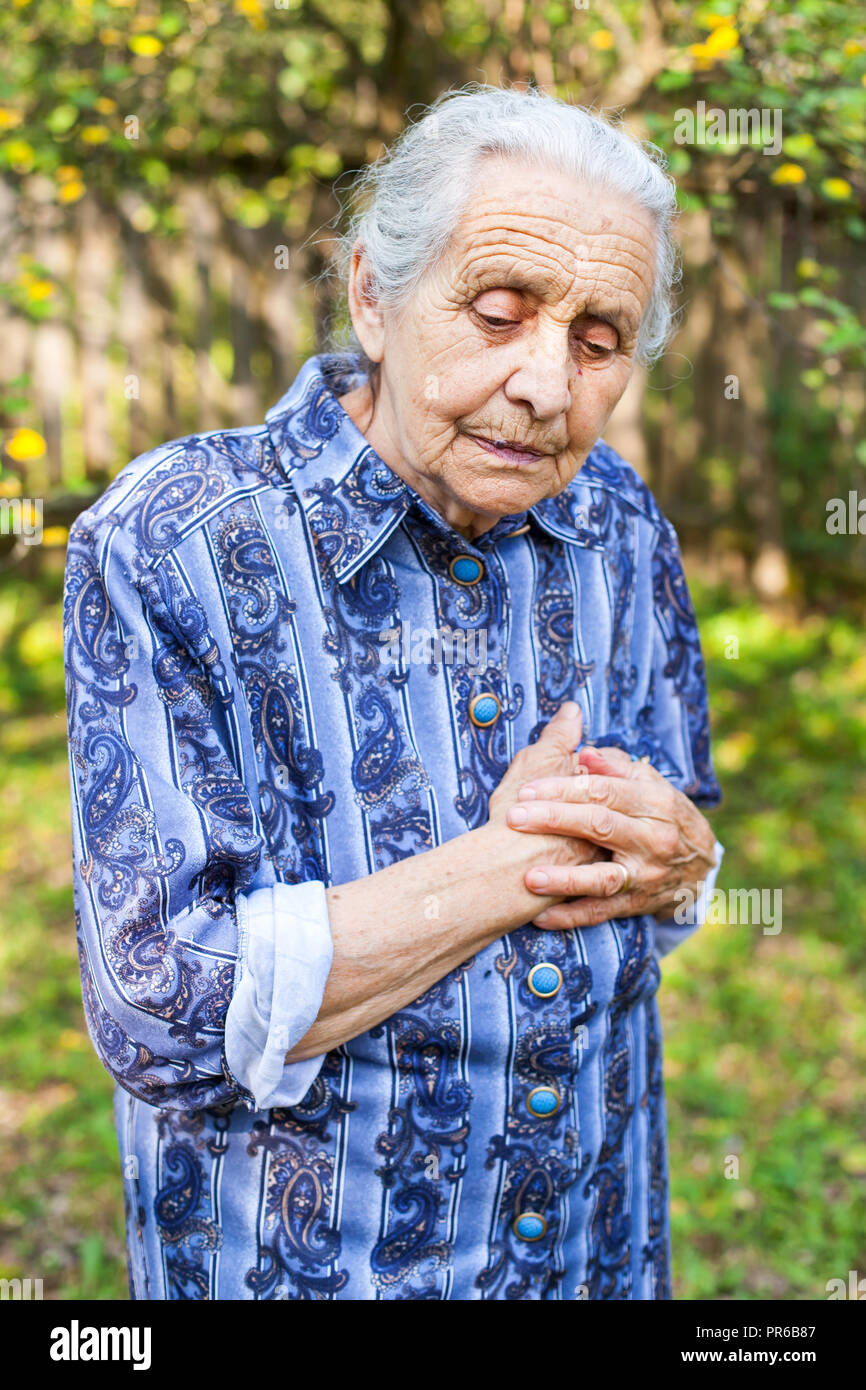 Portrait of old wrinkled lady wearing blue dress, walking in the garden on summertime Stock Photo