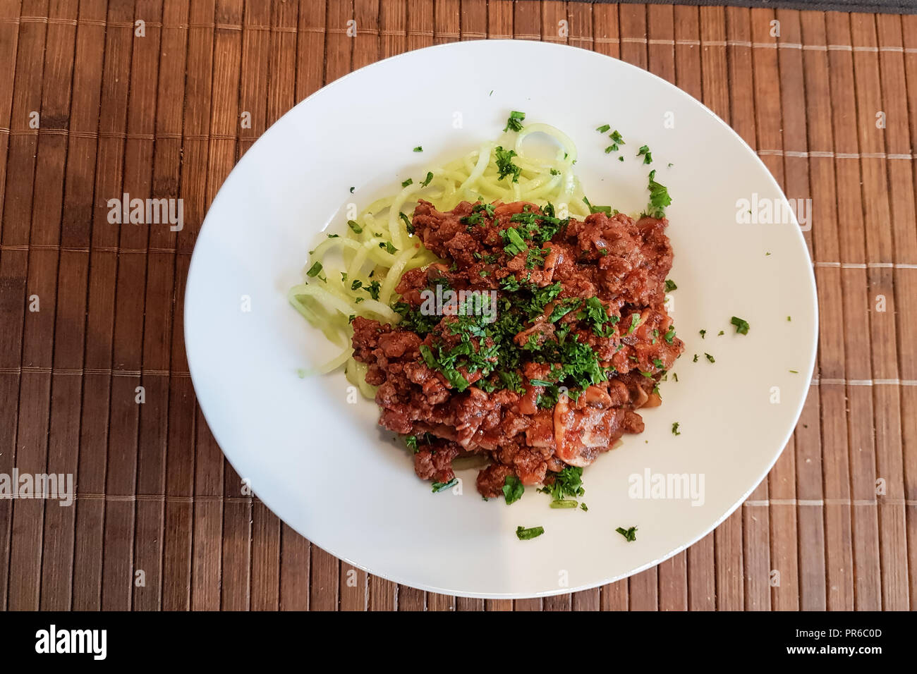 Healthy low carb food on white plate, lunch with snake cucumber in spaghetti strips cut above beef tartare with tomato sauce. Stock Photo