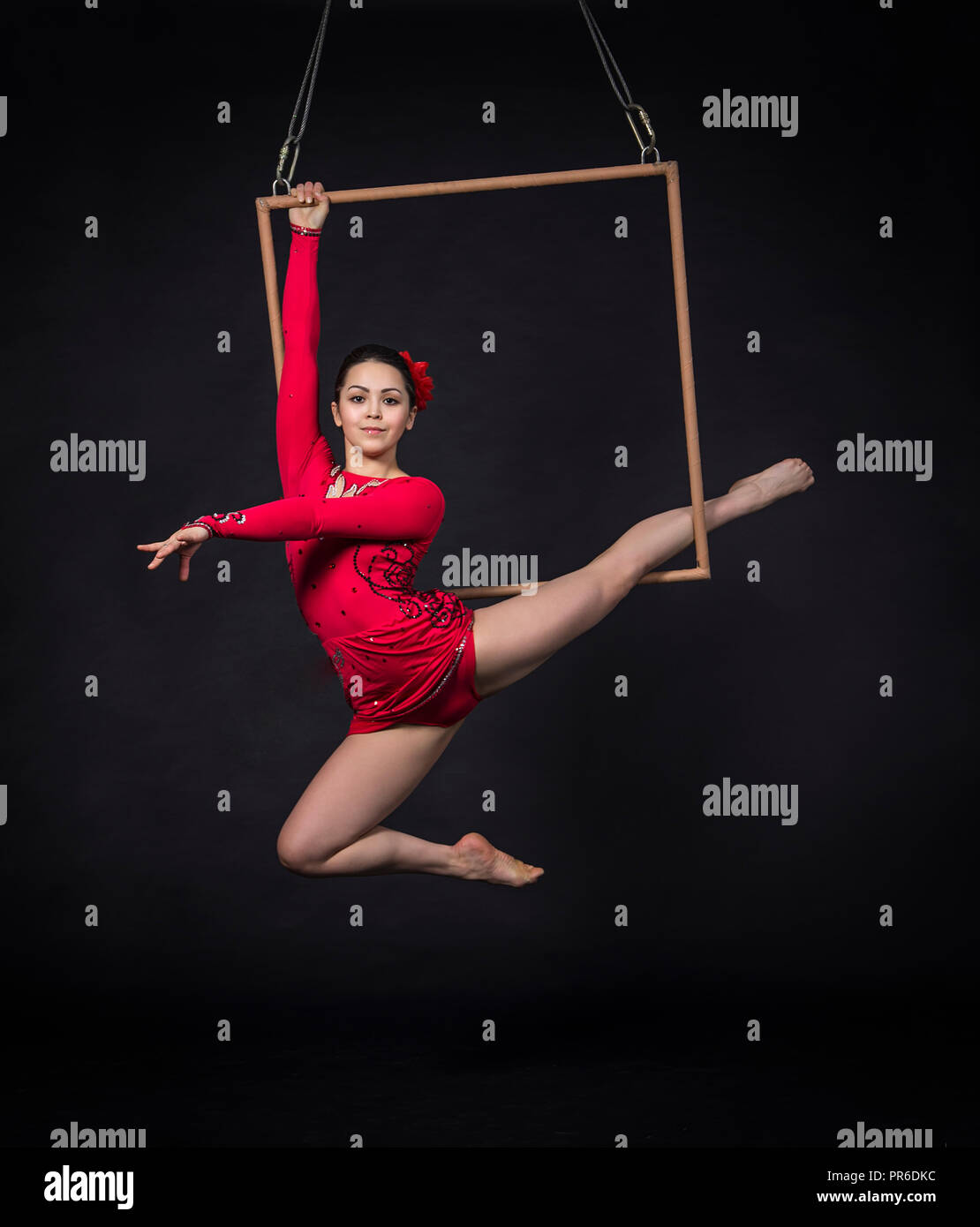 A young woman performs the acrobatic elements in the air trapeze. Studio shooting performances on a black background. Stock Photo