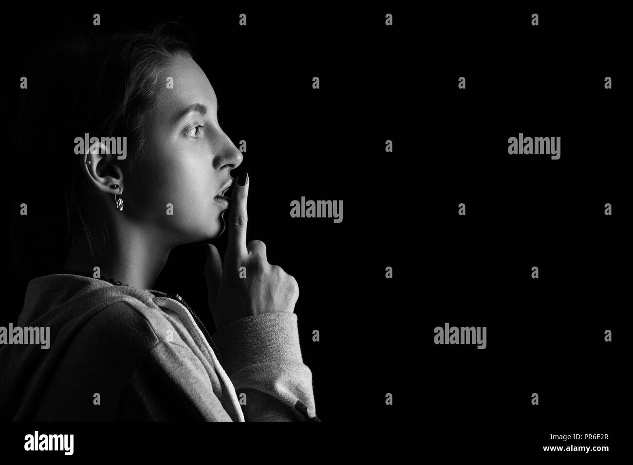 scared girl show silence gesture on black background with copy space, monochrome Stock Photo
