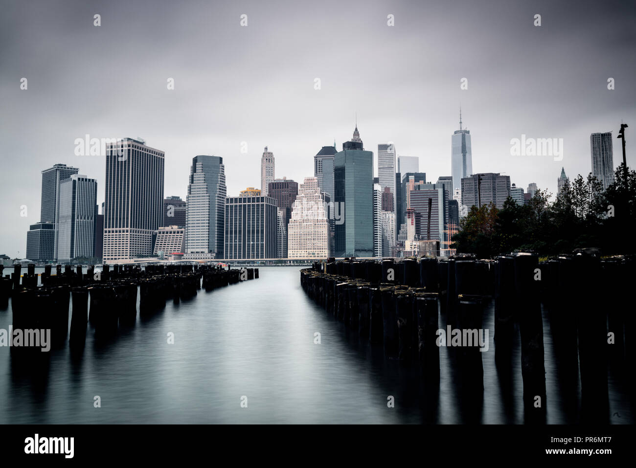 Long exposure shot of Manhattan's Financial District on a cloudy Summer morning, with old piers in the foreground. Desaturated, high contrast. Stock Photo