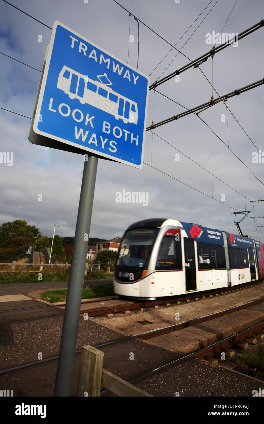 An Edinburgh tram passes by a caution sign as it makes its way over a pedestrian crossing point Stock Photo