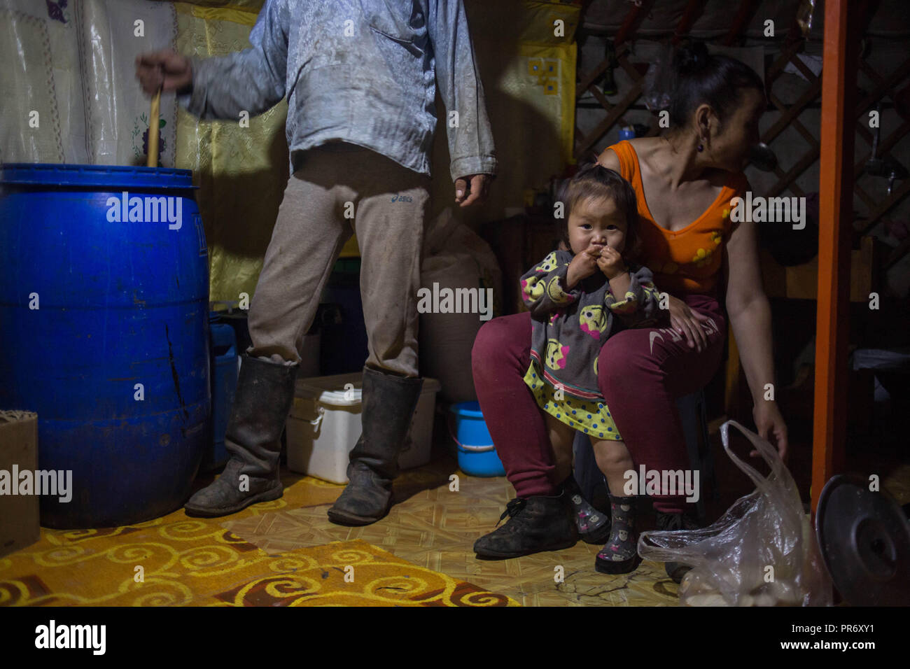 A local man seen preparing fermented horse milk inside a large tank during the evening while her wife seat next to him near the small town of Adaatsag in the Dundgovi Province in Central Mongolia. Stock Photo