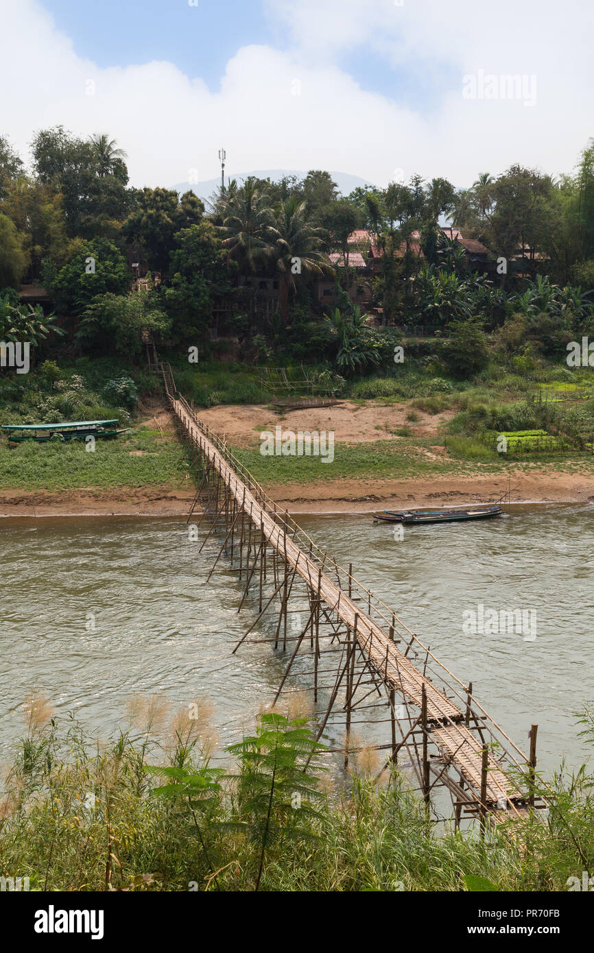 View of a bamboo bridge over Nam Khan River and lush riverbank in Luang Prabang, Laos, on a sunny day. Stock Photo