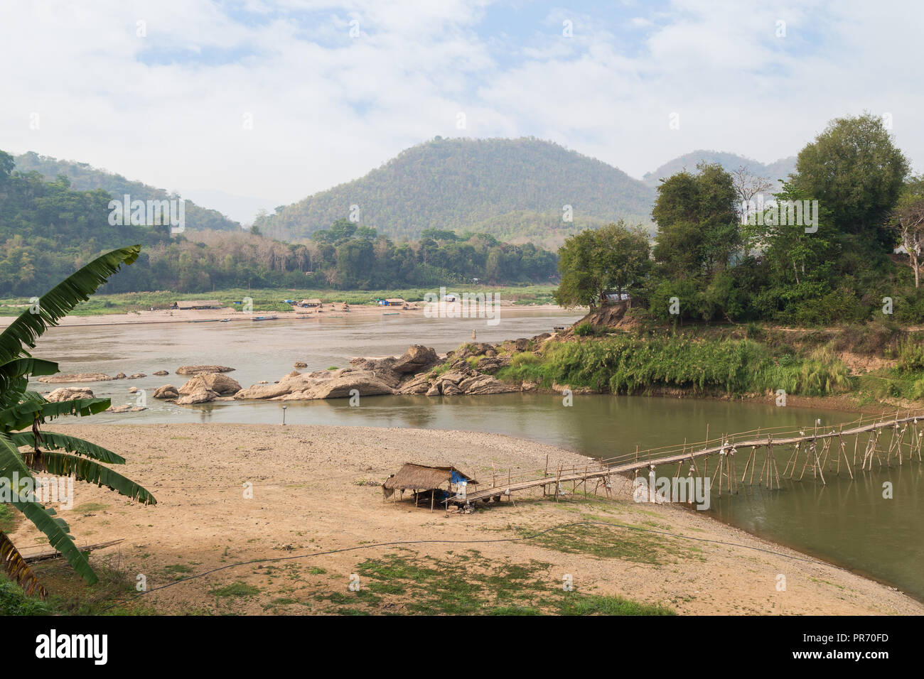 View of Mekong River, a bamboo bridge over Nam Khan River at low tide and lush riverbank in Luang Prabang, Laos, on a sunny day. Stock Photo