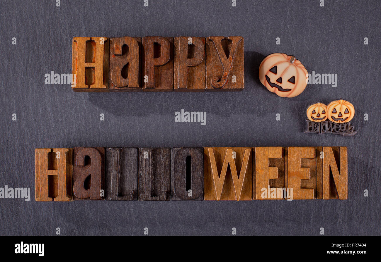 Happy Halloween text written in wooden block letters with pumpkin icons on a black background Stock Photo