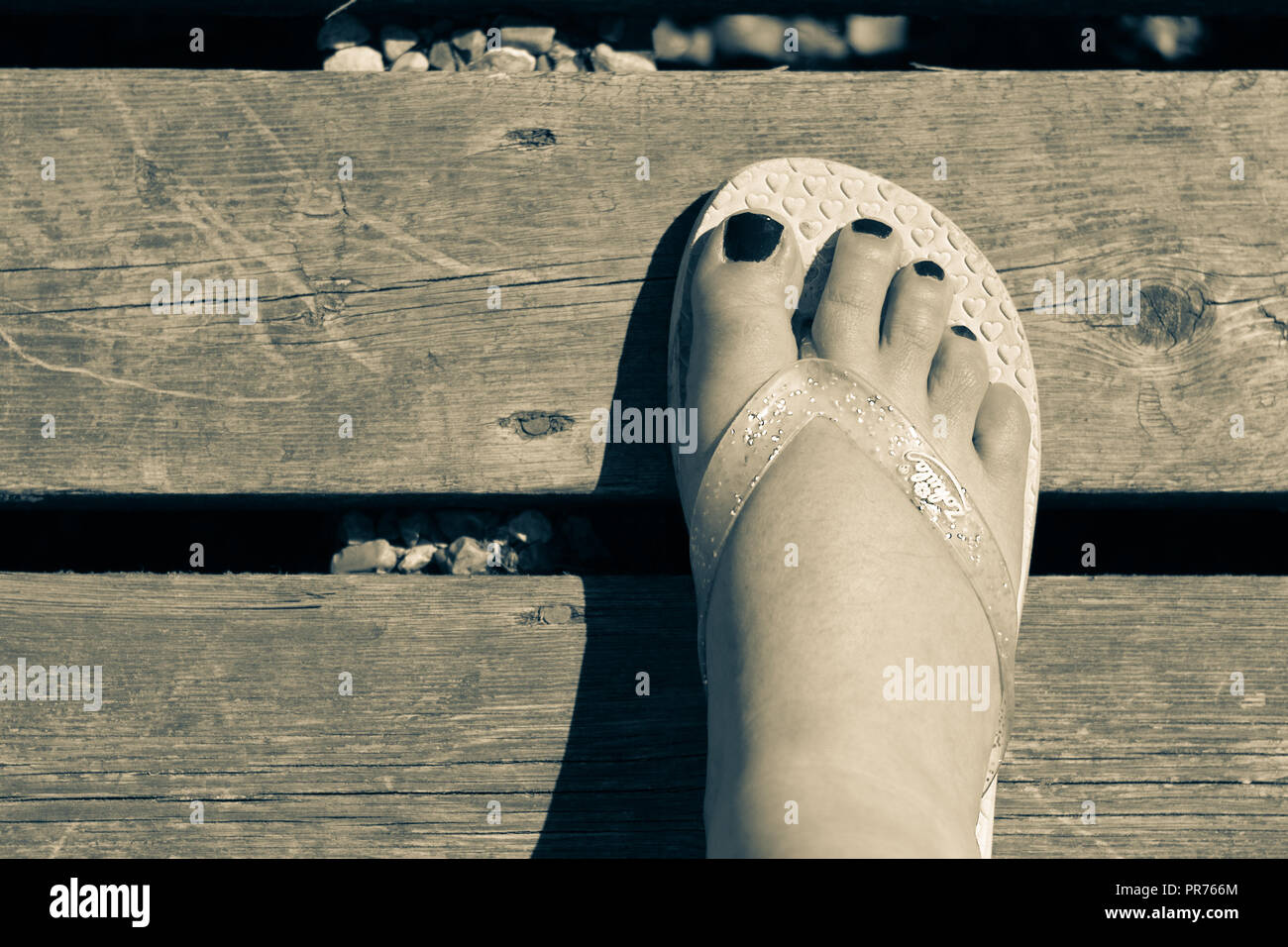 Close up of a foot wearing a flip flop standing on  a wooden boardwalk Stock Photo