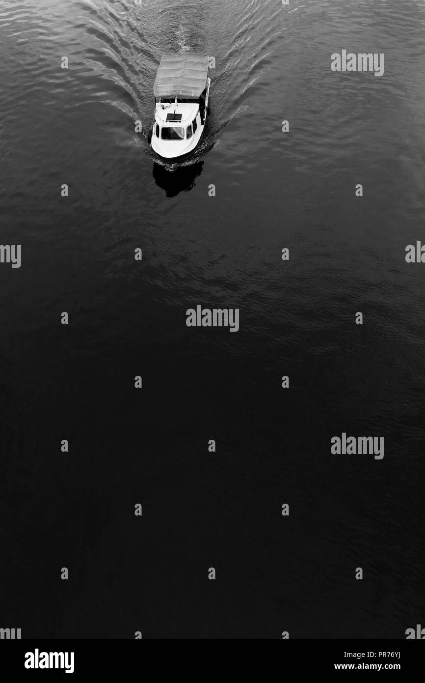 Very minimalistic picture in black and white showing a boat cruising on the river Stock Photo