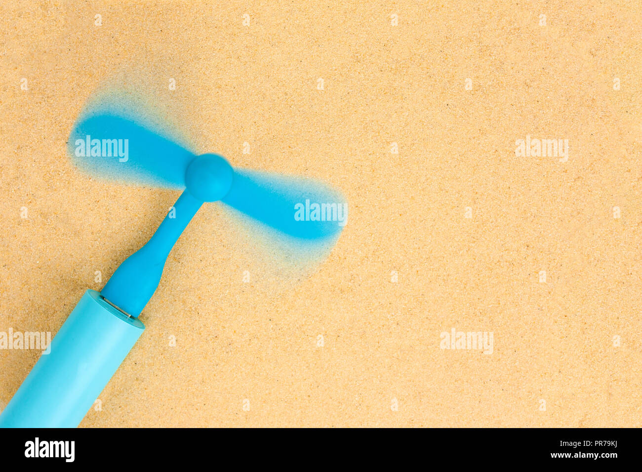 The blue portable fan is inserted into the blue power bank and lies on the sand.Top view. Stock Photo