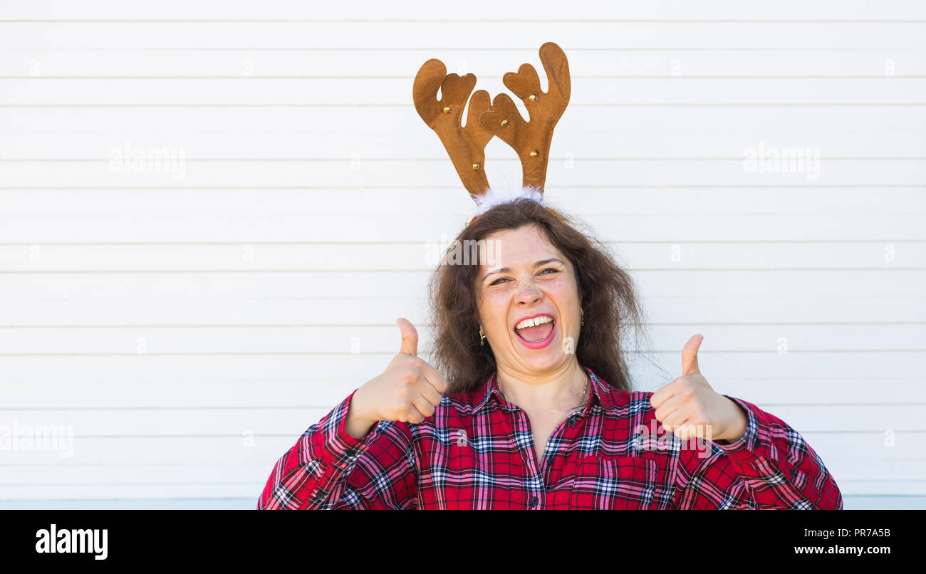 Happy beautiful woman in Christmas costume with deer horns on her head gesturing thumbs up over white background with copy space Stock Photo