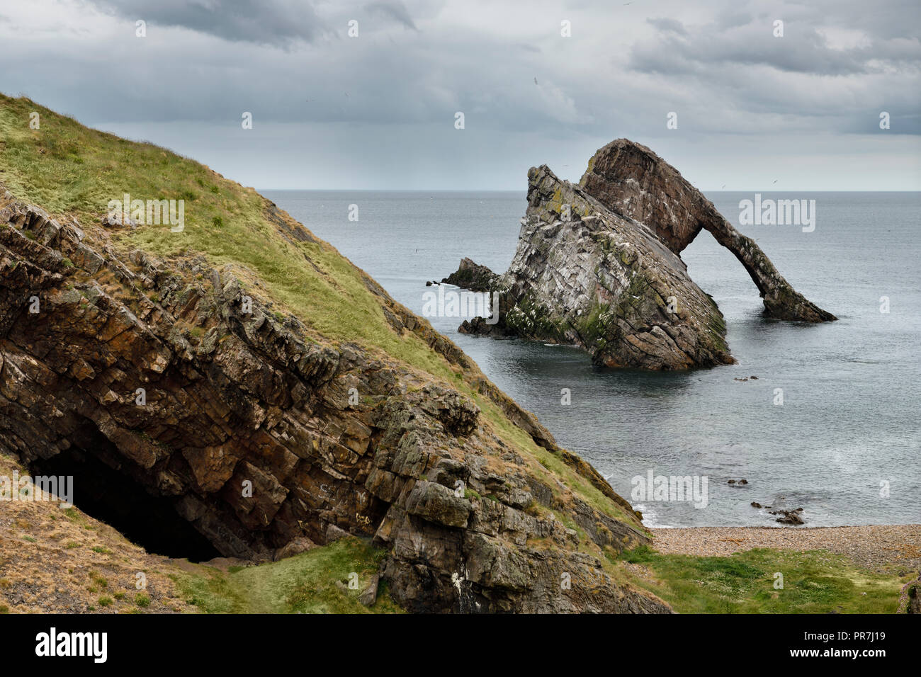 Cave and Bow Fiddle Rock quartzite sea arch with pebble beach at Portknockie on the North Sea Atlantic ocean Scotland UK Stock Photo