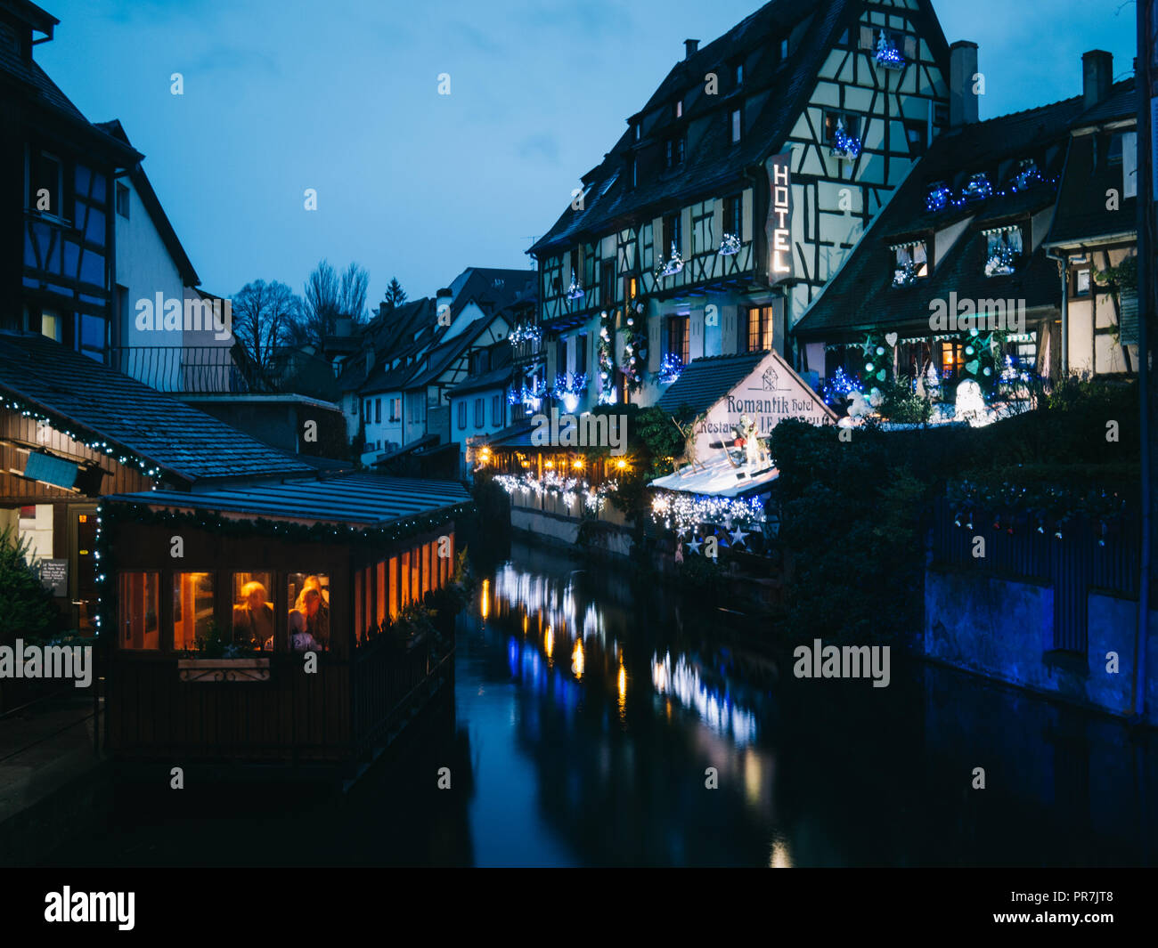 View a bridge in Strasbourg, France at night with different lights and windows over a river with boats. Christmas time Stock -