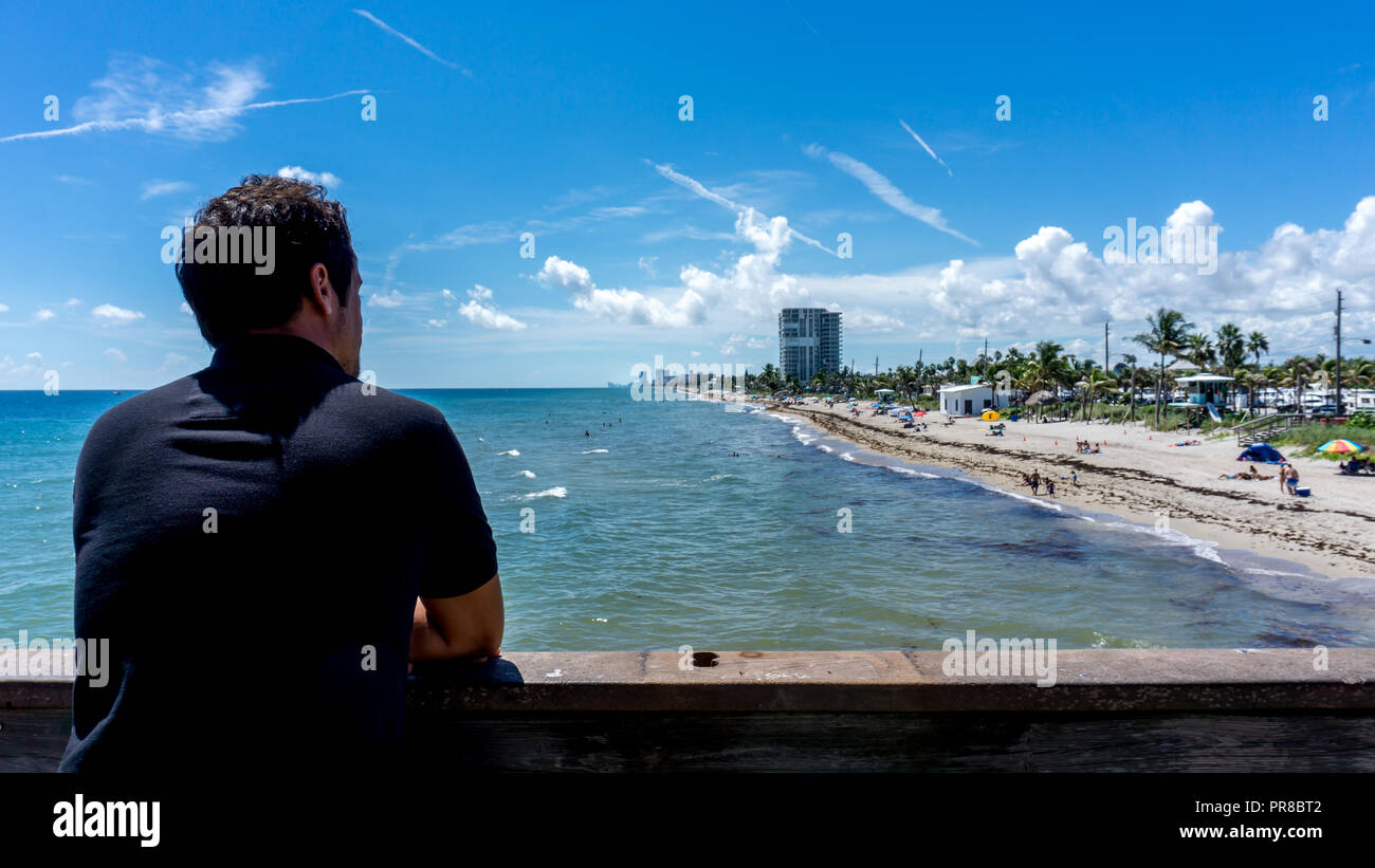 Young man looking at the view of Dania beach in Miami, Florida. Summer sunny day with many people swimming in the water Stock Photo