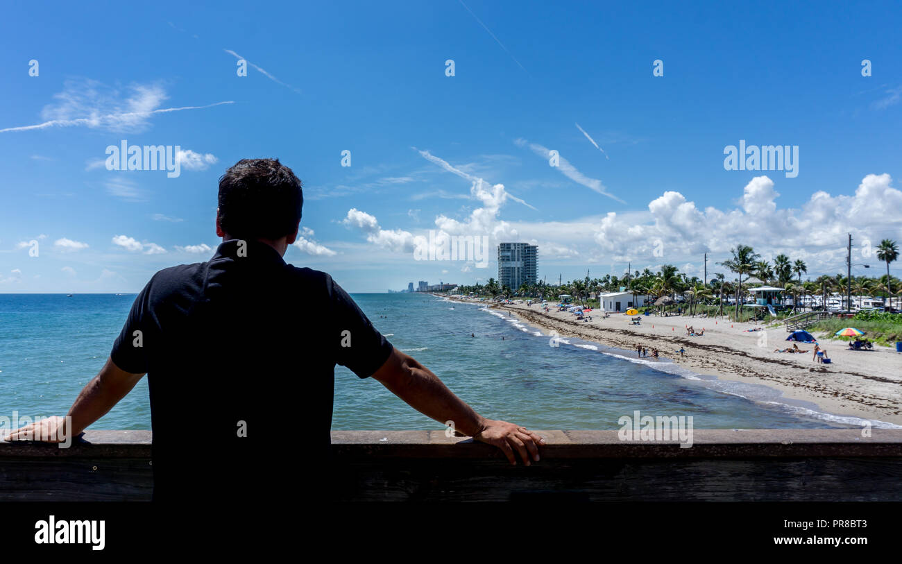 Young man looking at the view of Dania beach in Miami, Florida. Summer sunny day with many people swimming in the water Stock Photo