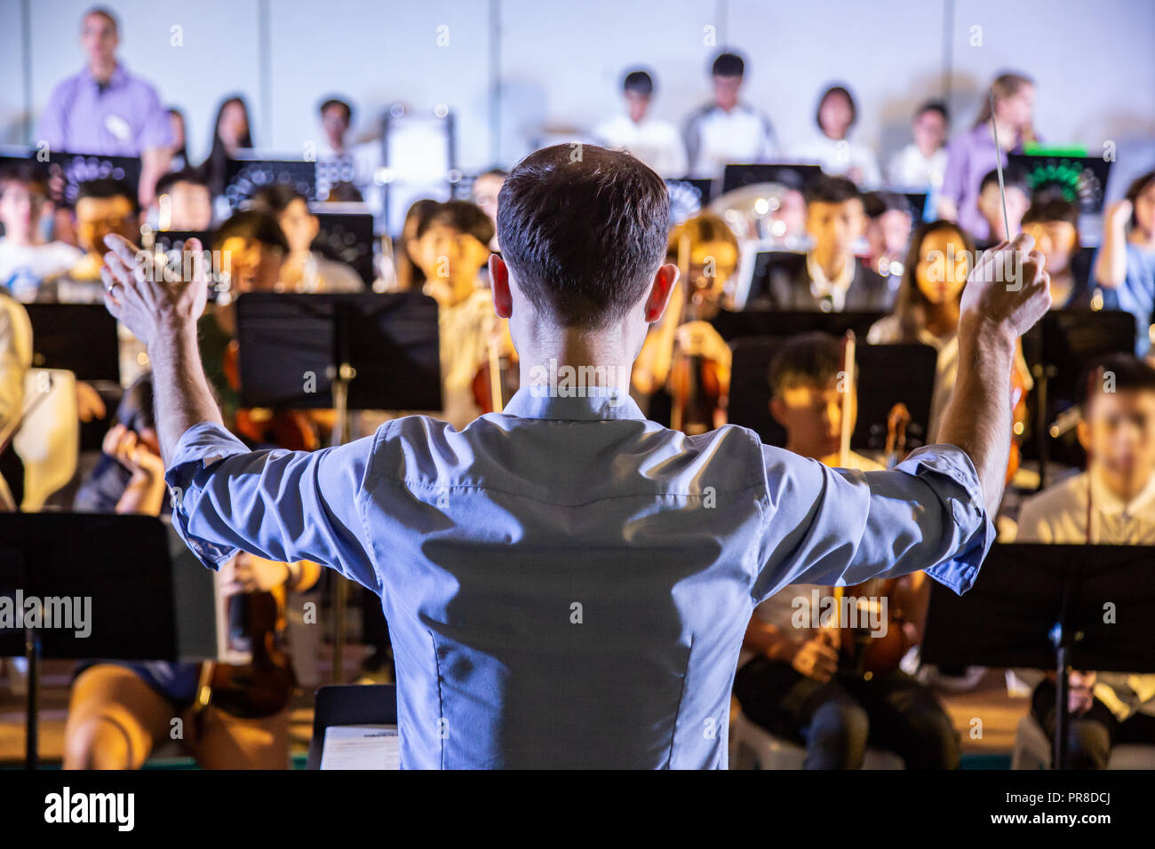 Male school conductor conductiong his student band to perform music in a school concert Stock Photo