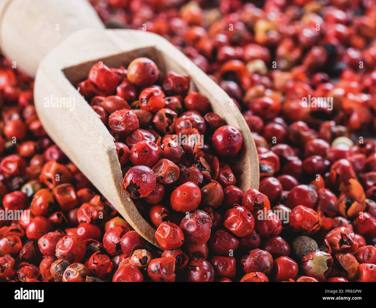 Wooden scoop filled with dried pink pepper berries. Close up view of pink peppercorn. Stock Photo