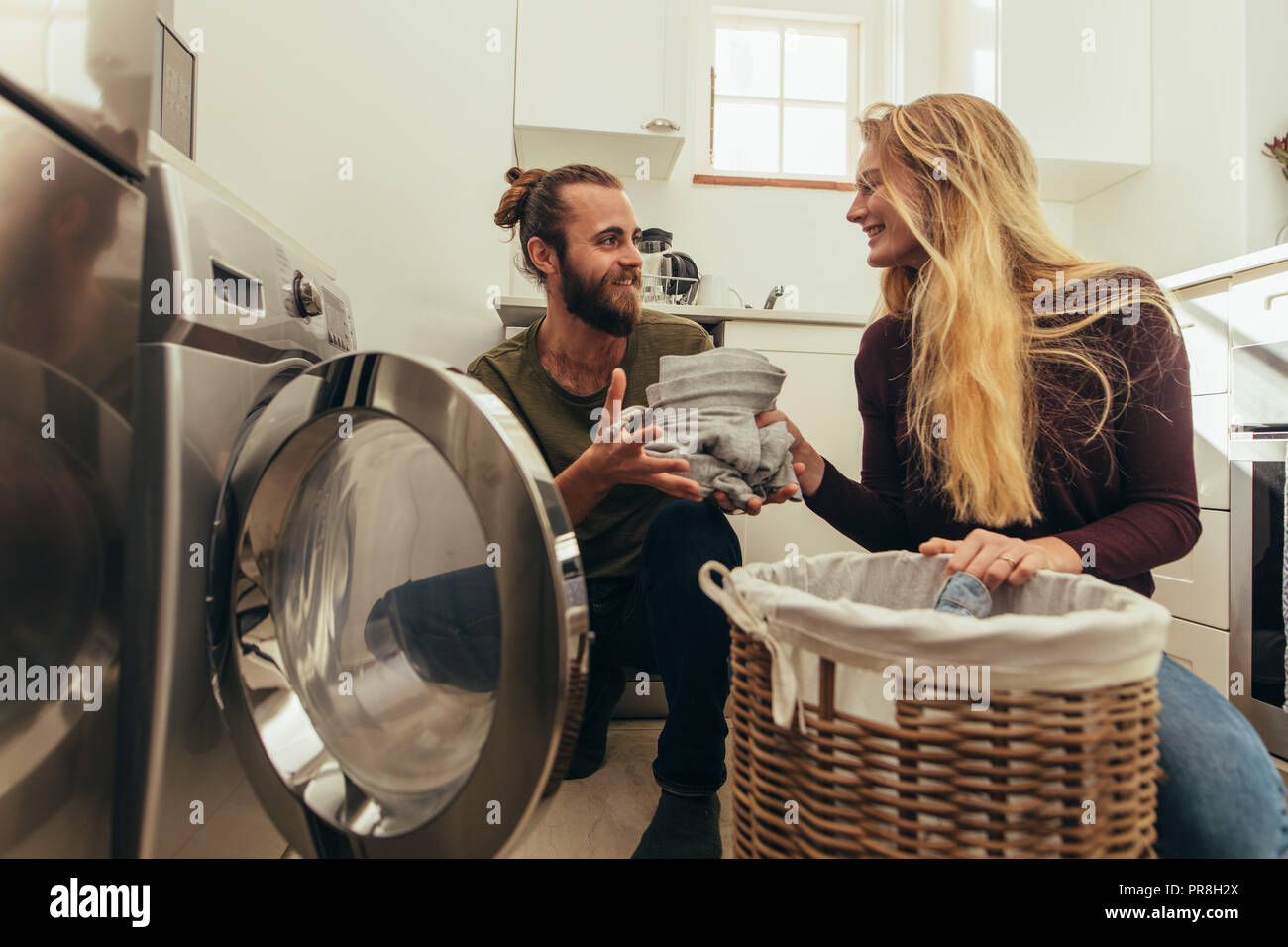 Happy couple putting clothes in washing machine. Couple using a front loading washing machine to wash laundry. Stock Photo