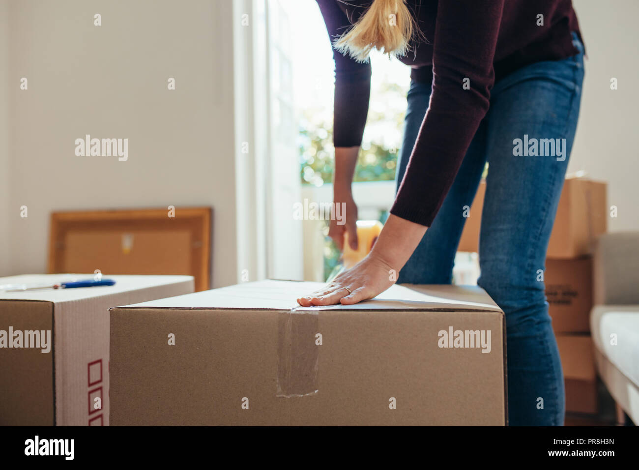 Woman using adhesive tape to seal the packing boxes. Woman moving out to a new home packing household stuff in packing boxes. Stock Photo