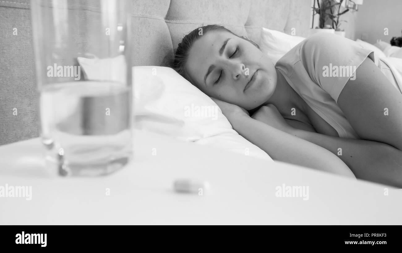 Black and white image of young woman feeling unwell lying in bed Stock Photo