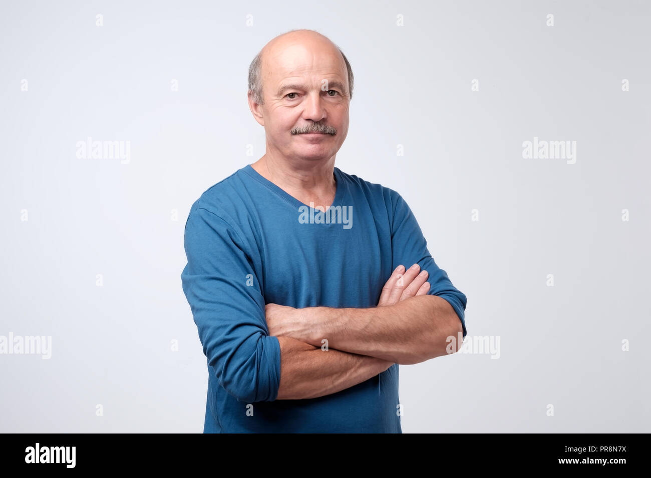 Portrait of mature european man with mustache in blue shirt having his arms crossed, looking at camera Stock Photo