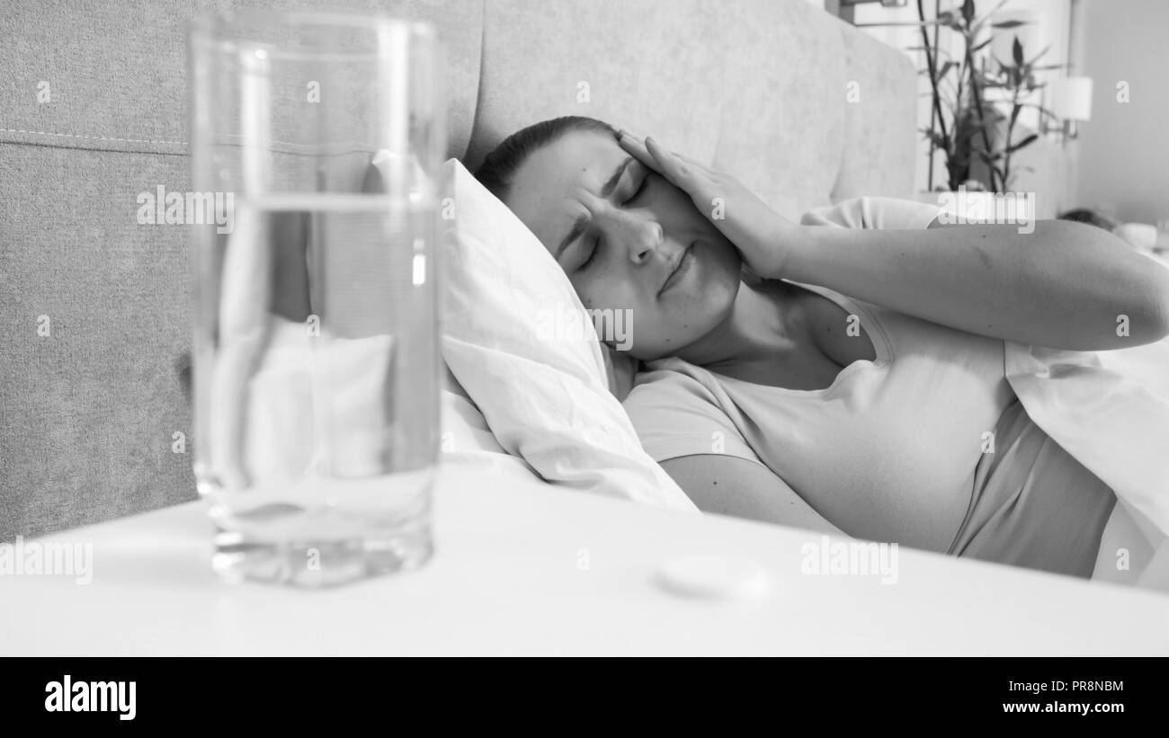 Black and white portrait of young woman suffering from headache lying in bed Stock Photo