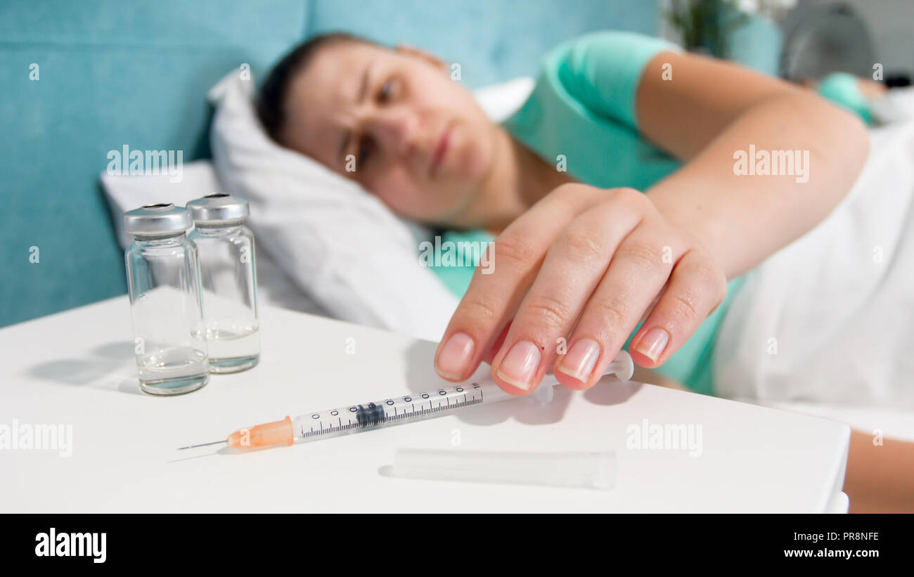 Closeup photo of young sick woman taking syringe with painkiller medicine from bedside table Stock Photo