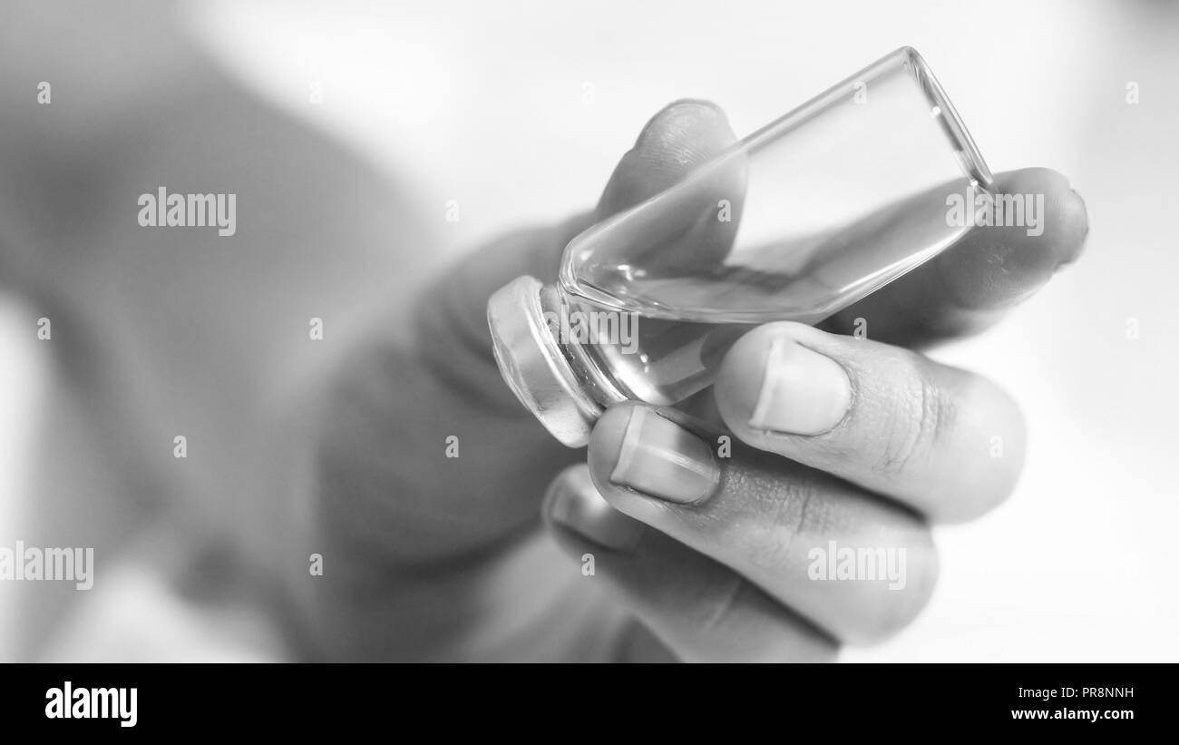 Black and white image of female hand holding ampule with medictaion